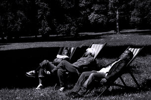 Black and white video still of Liryc Dela Cruz' film ›Come La Notte‹ (2025). Three people laying on loungers in a park enjoying the sun.