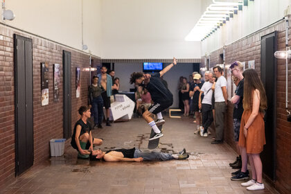 En Skater spring mit seinem Skateboard über eine liegende Person im Flur von PACT Zollverein