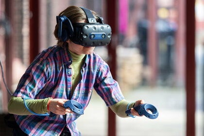 One person has put on VR goggles and is holding two controllers in their hands. 