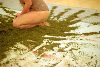 Die Künstlerin sitzt mit Farbe beschmiert auf einem Haufen Erde.