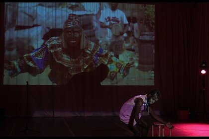 Emmanuel Ndefo hockt vor einer Leinwand mit einer Fotografie von einem performenden Mann