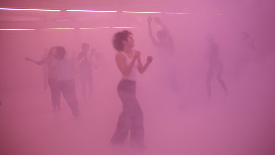 Eine Gruppe Menschen tanzt in pink beleuchtetem Nebel