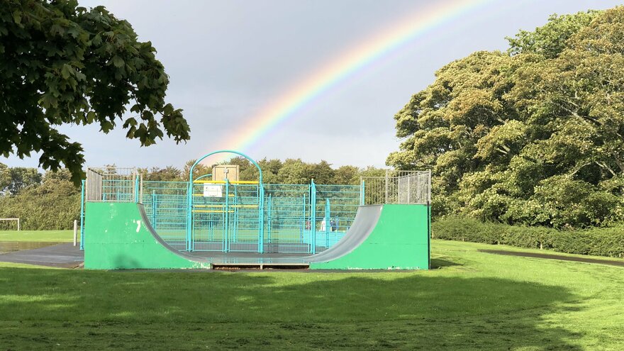 Foto von einer Skateanlage im Grünen über die ein Regenbogen scheint