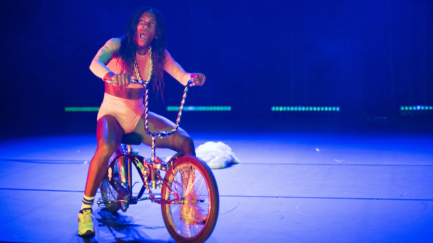 Eine Schwarze Frau in orangenem Kostüm auf einem BMX Rad